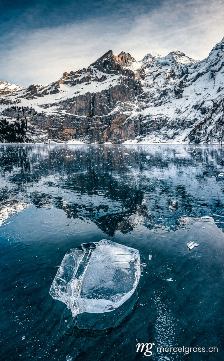 Winter picture Switzerland. beaufiful clear chunk of ice on frozen lake Oeschinensee with reflection and Blümlisalp Mountains in the Bernese Alps. Marcel Gross Photography