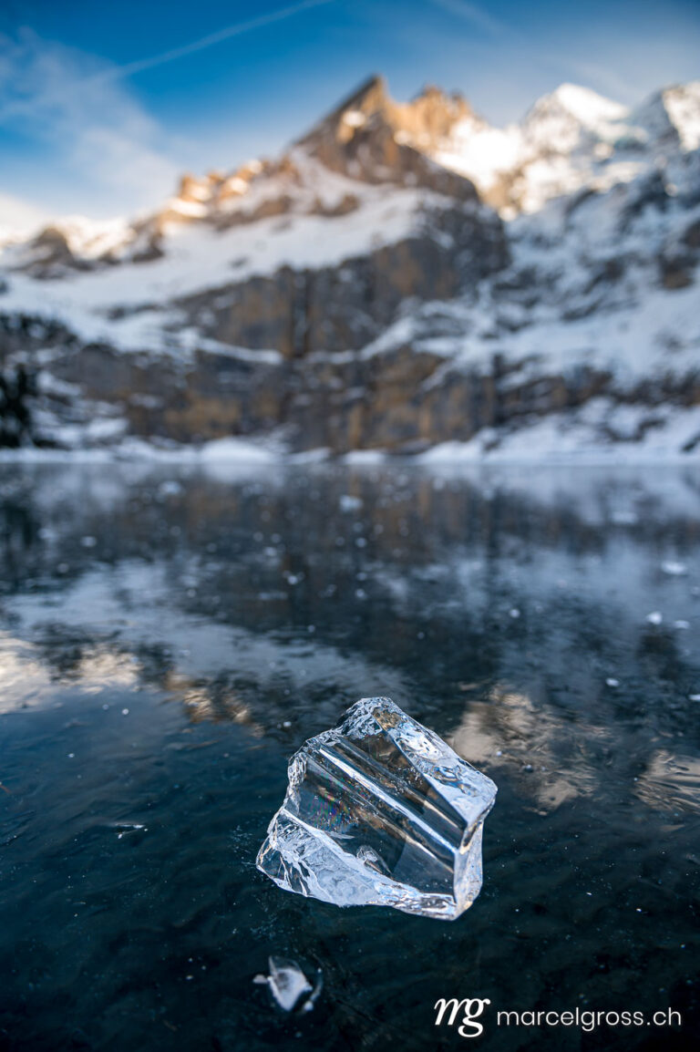 . beautiful clear chunk of ice on frozen lake Oeschinensee with reflection and Blümlisalp Mountains in Berner Oberland. Marcel Gross Photography
