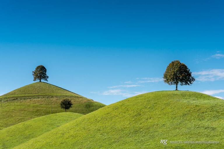 green hills with trees on top against blue sky. Taken by Marcel Gross Photography