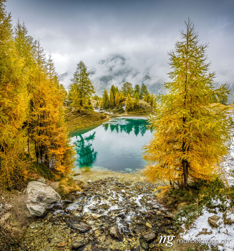 Autumn picture Switzerland. Yellow larches at a blue mountain lake in Valais. Marcel Gross Photography