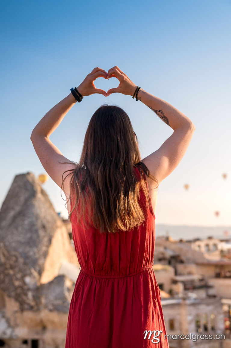 cappadocia pictures. girl in red dress forming a heart with hands. Marcel Gross Photography