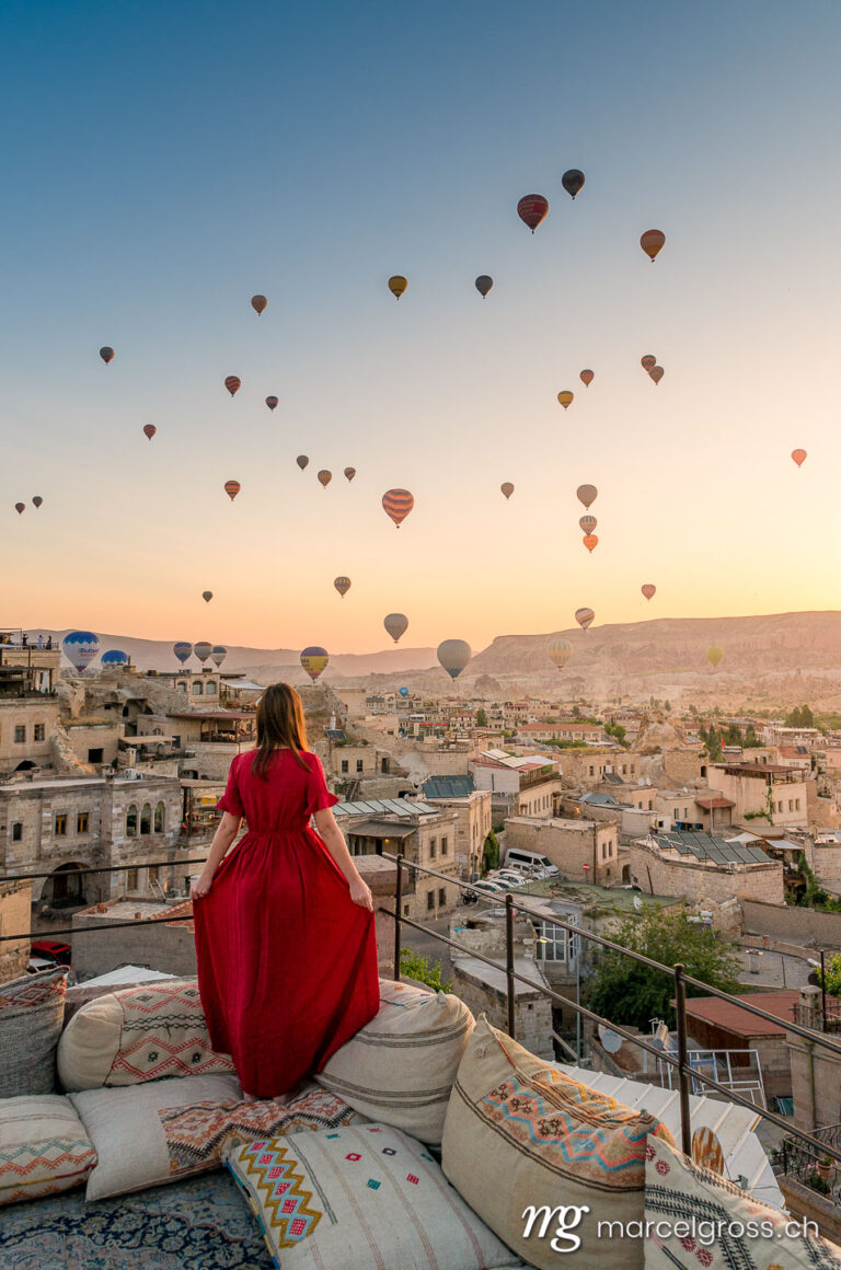 cappadocia pictures. girl in red dress with a balloon filled sky in Cappadocia. Marcel Gross Photography