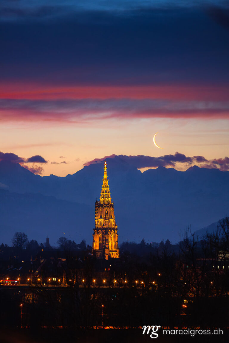 Bern Bilder. Berner Münster mit Mondsichel und Jungfrau während eines Sonnenaufgangs. Marcel Gross Photography